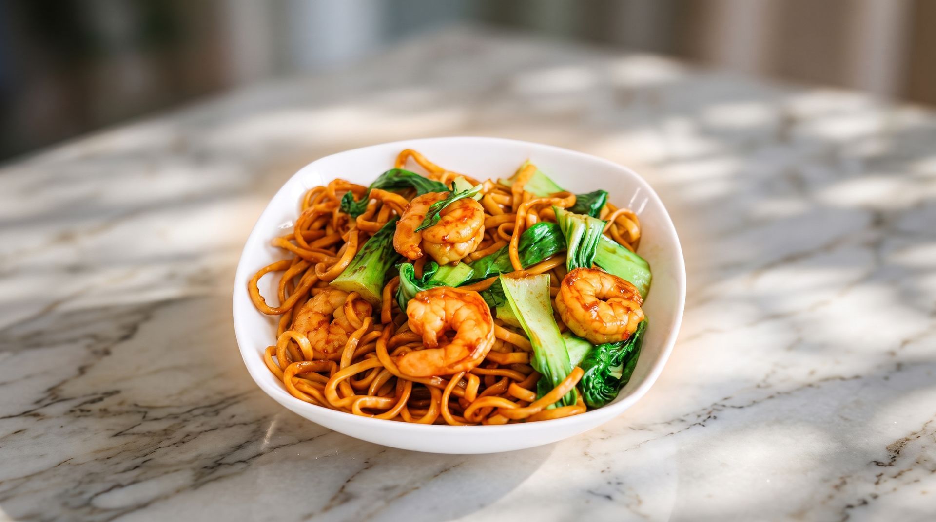 White bowl of noodles with broccoli and shrimp on a marble table outdoors in sunlight