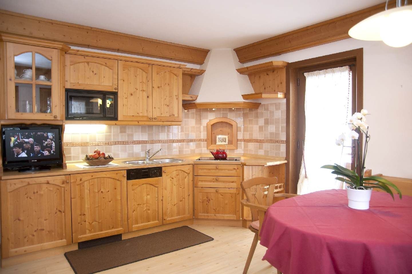 Bright kitchen with wooden cabinets, tiled backsplash, and a table with a pink tablecloth and flower vase