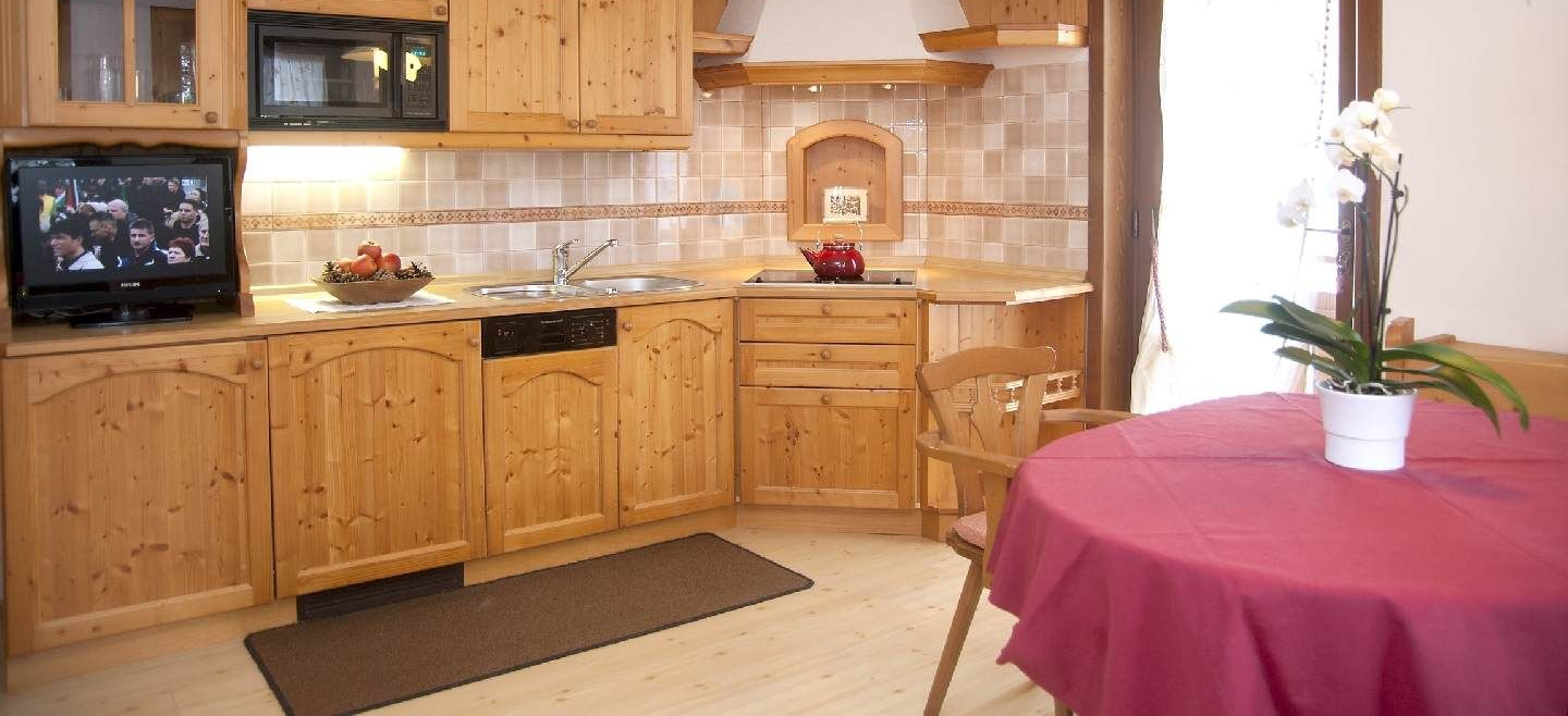 Cozy kitchen with wooden cabinets, tiled backsplash, and a round table draped in a red tablecloth.