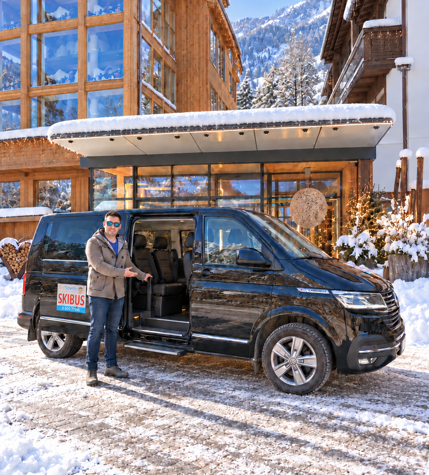 Person standing by a black van in a snowy mountain resort driveway with lodge buildings behind.