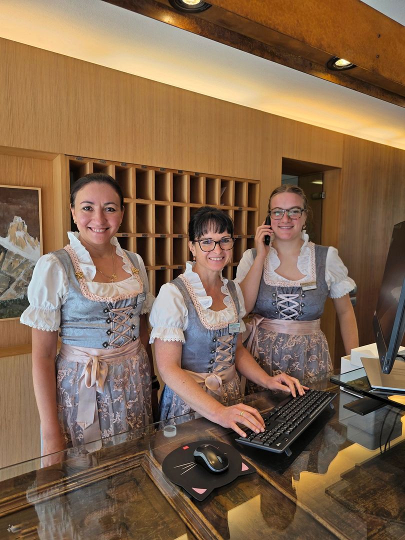 Three smiling staff behind a hotel reception desk in matching aprons and white blouses