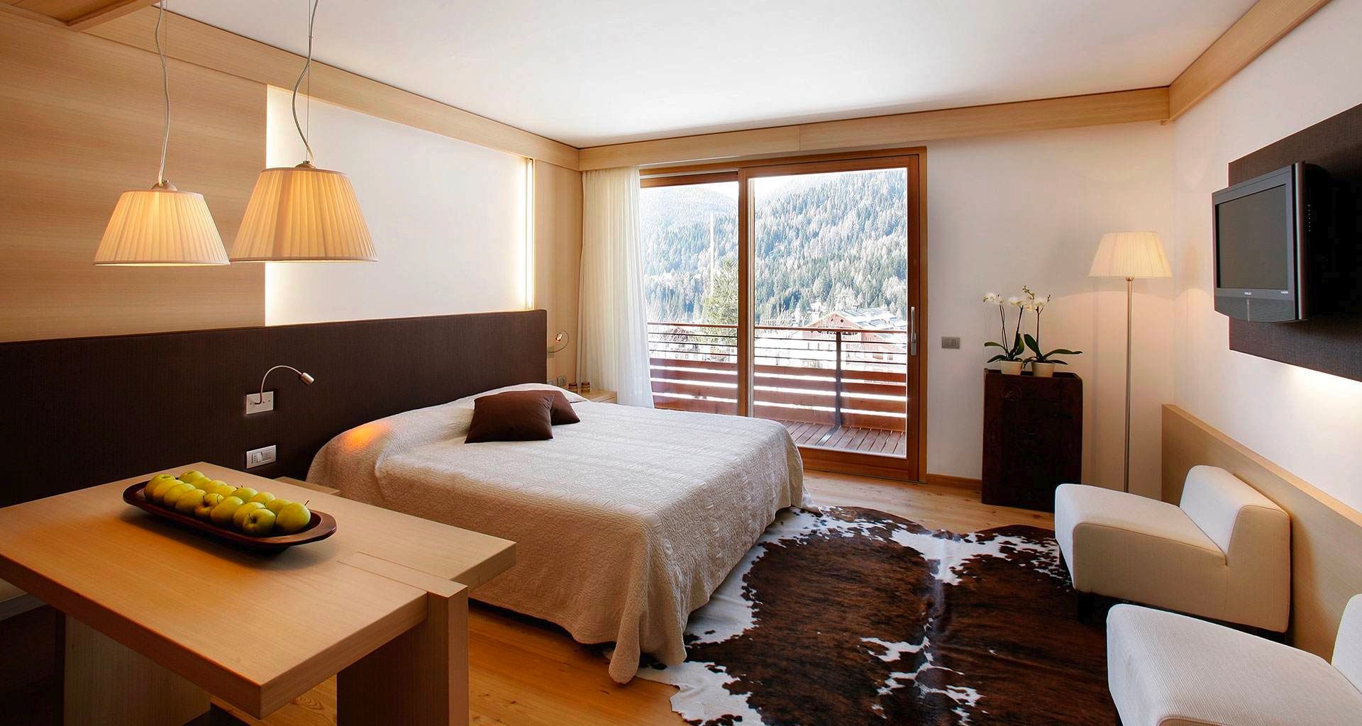 Cozy hotel room with a bed, lamps, chairs, and balcony view of snowy mountains