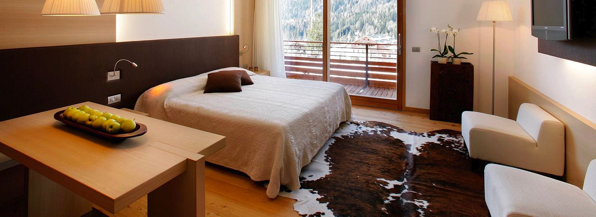 Modern bedroom with a bed, desk, chair, and large window overlooking trees and snow