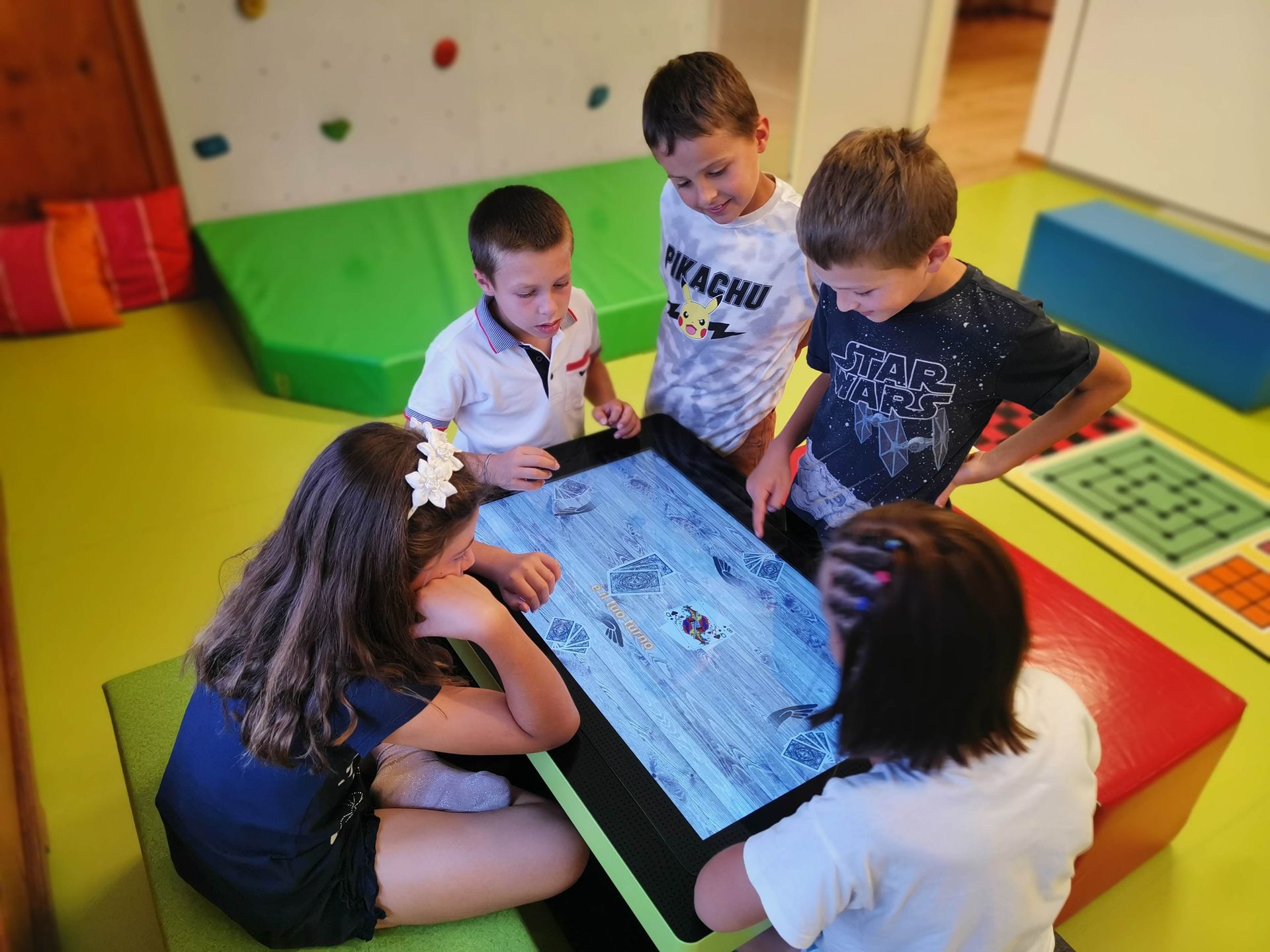 Children gathered around a tablet on colorful classroom cushions, collaborating and looking at the screen