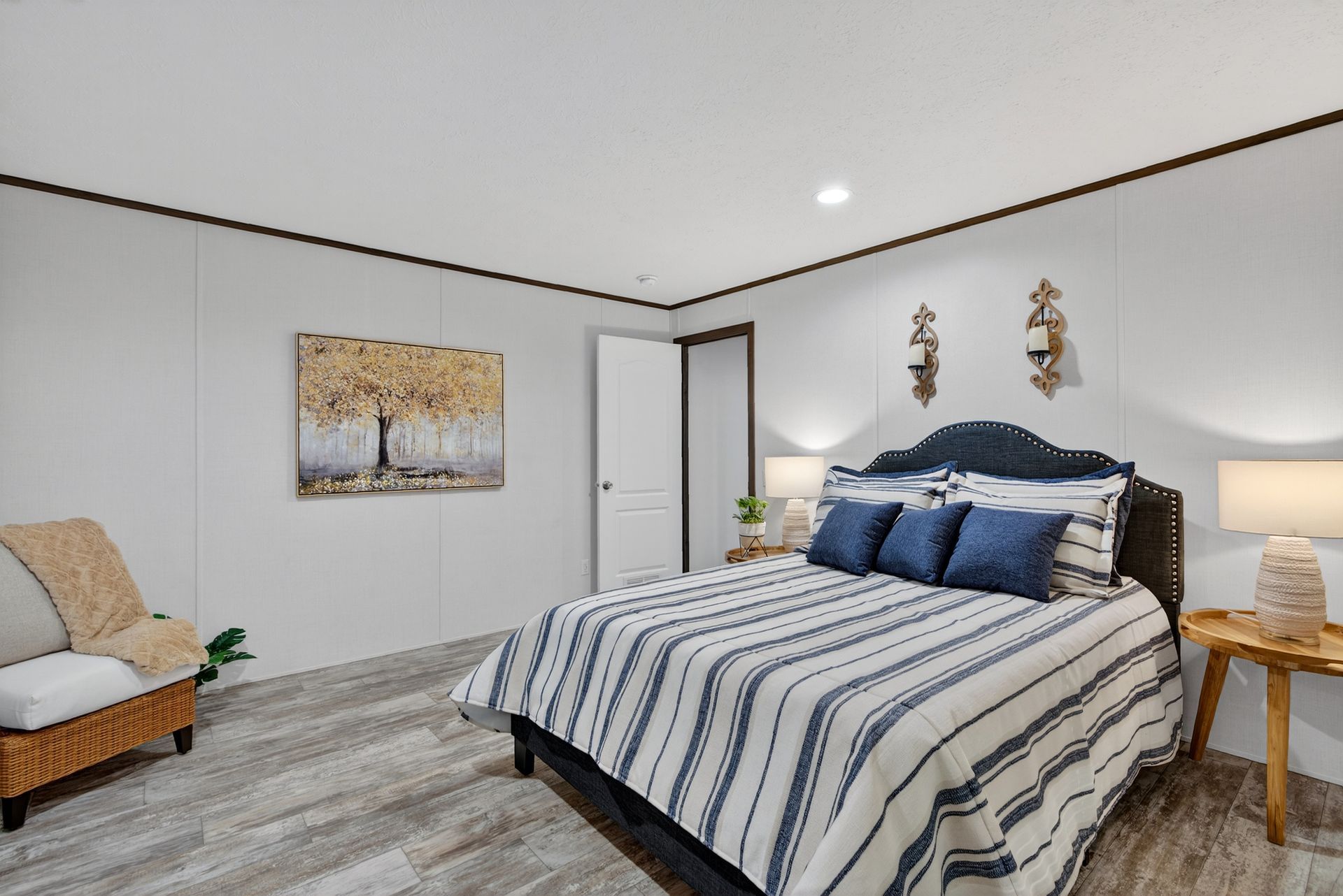 Bright bedroom with a striped bedspread, white walls, a chair, nightstand, and wall art