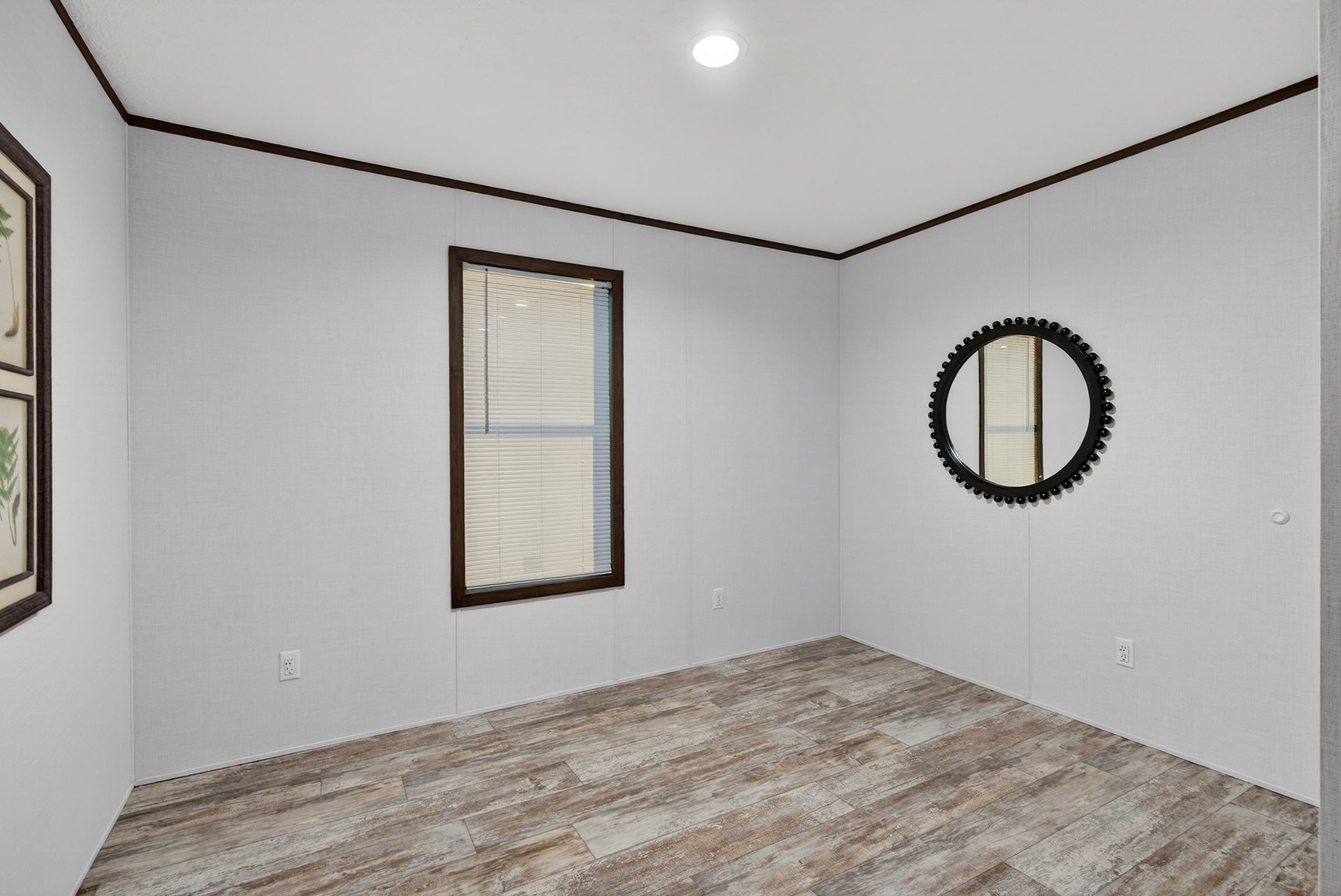 Empty white room with wood floor, two windows, and a round wall mirror.