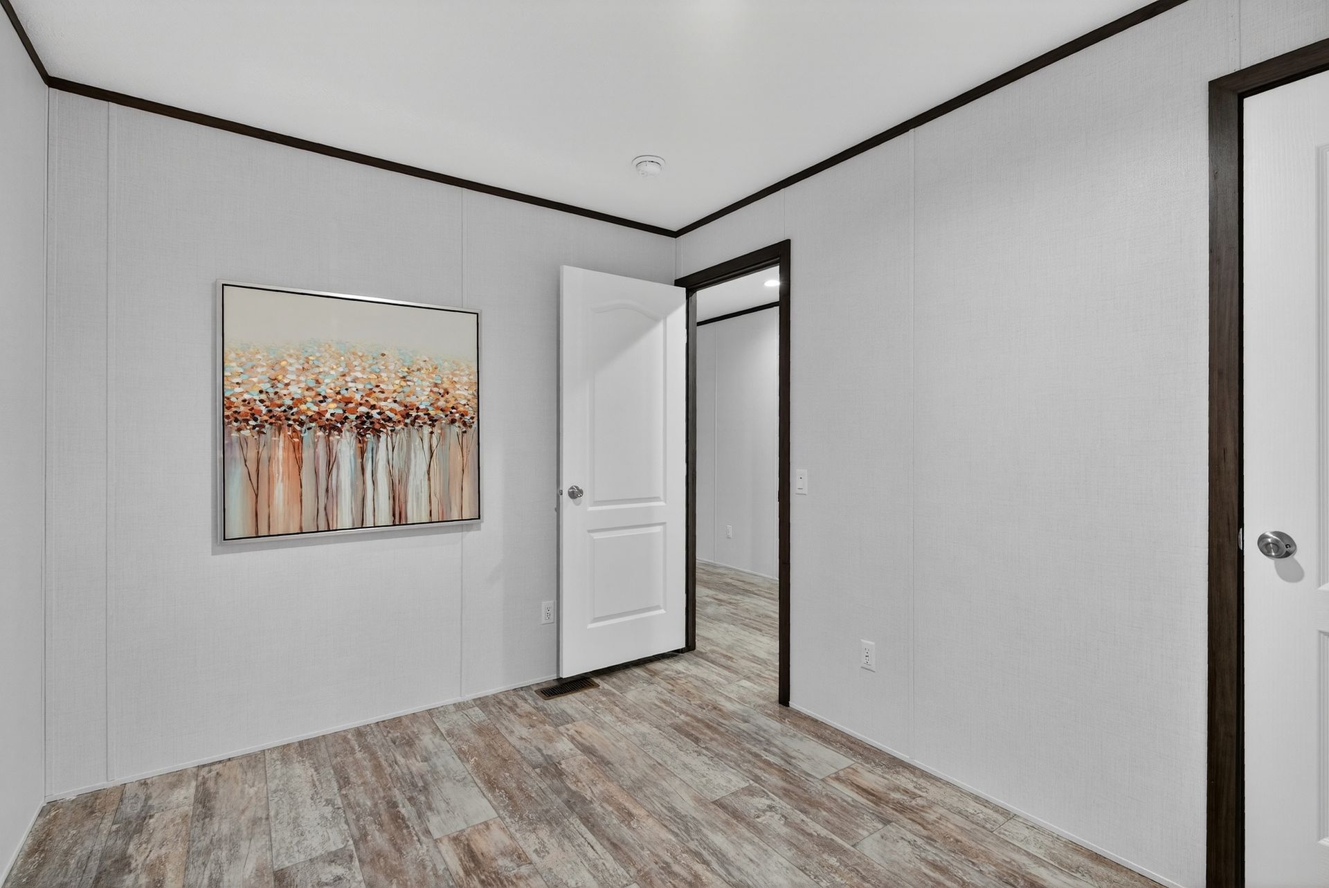 Empty bedroom with gray walls, wood floor, open door, and abstract wall art.