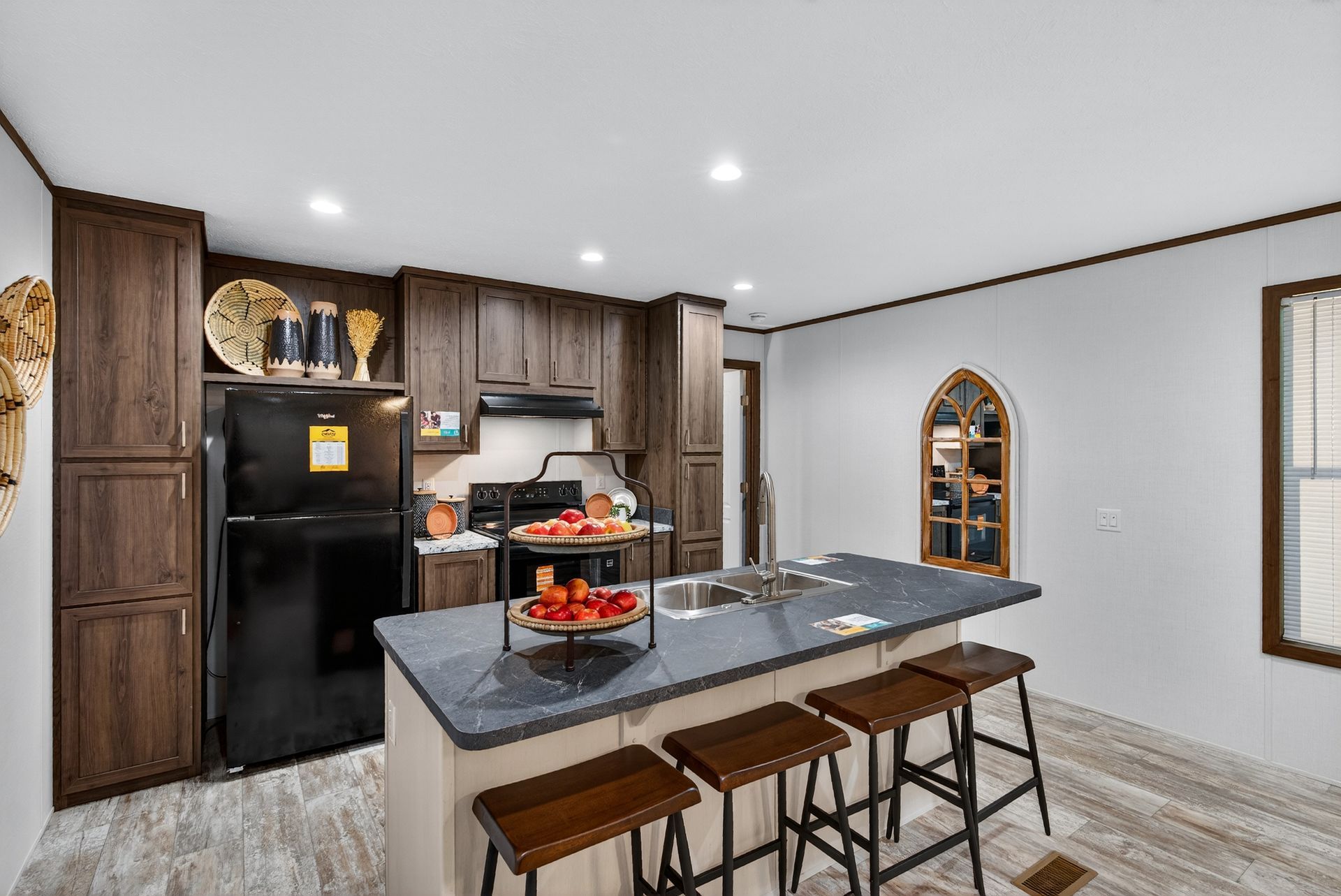 Modern kitchen with dark wood cabinets, black fridge, and a center island with stools and pastries.
