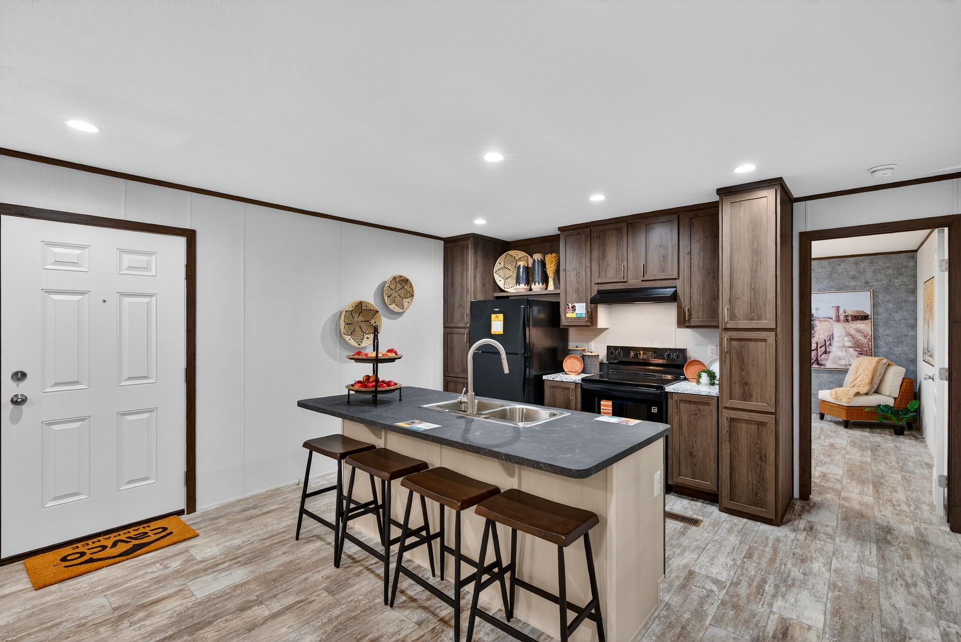 Modern kitchen with island seating, dark cabinets, and a white front door opening to a hallway