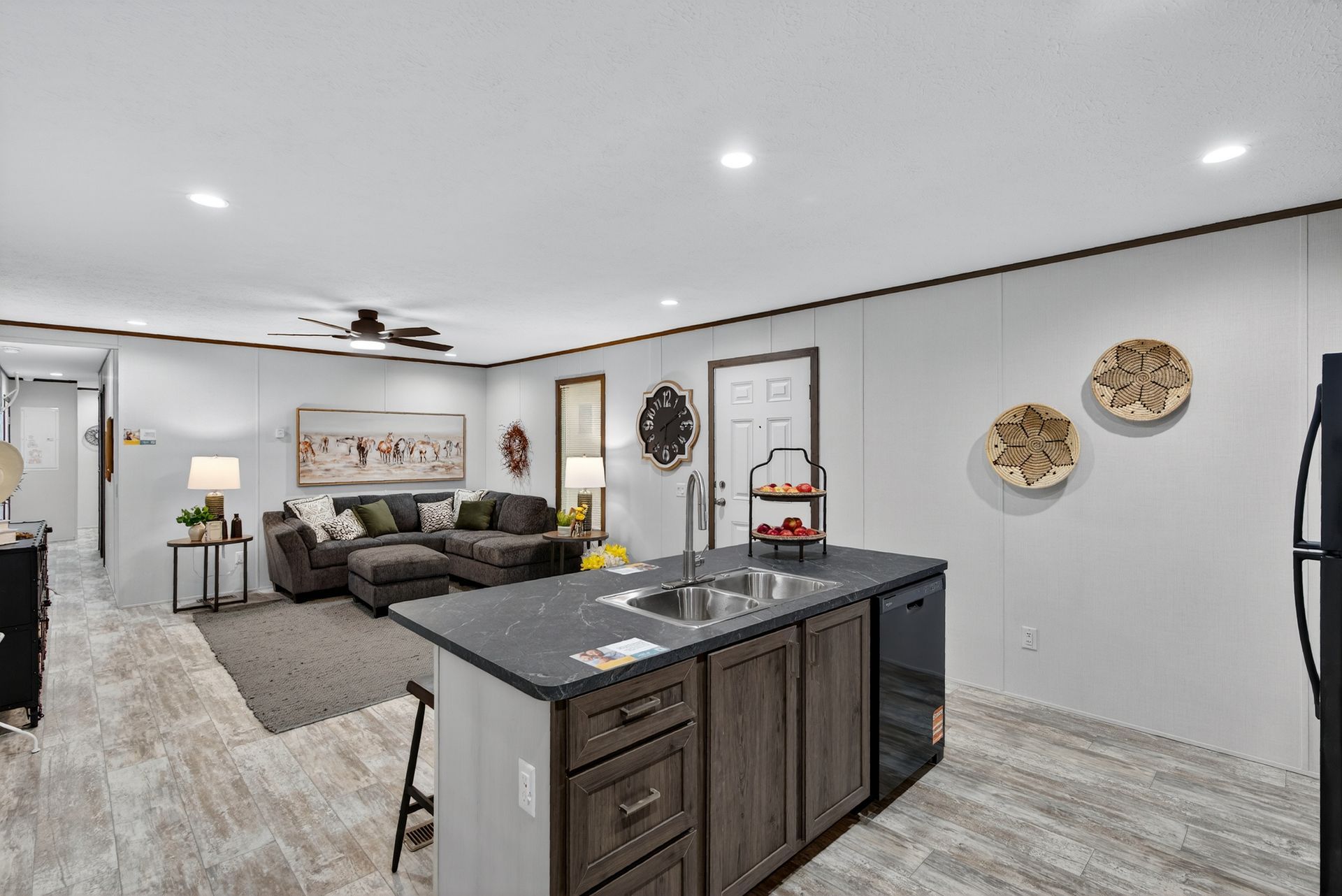 Modern open-concept kitchen and living room with gray cabinets, island, sectional sofa, and wall decor.