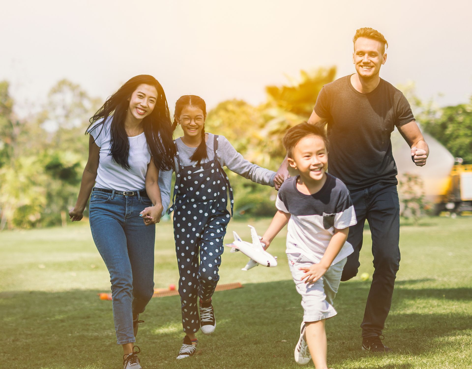 Four people running and smiling together on a sunny grassy field