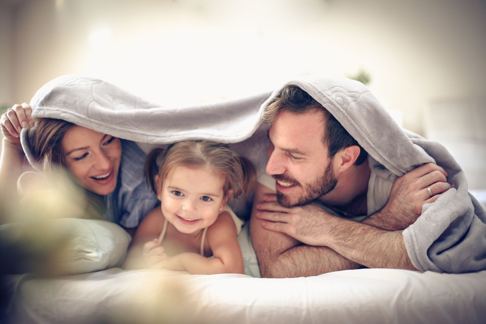 Family under a blanket, smiling and cuddled together on a bed