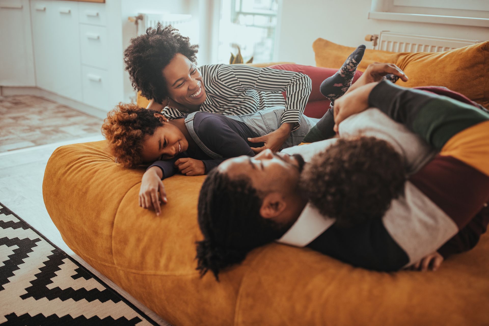 Three people relaxing together on an orange beanbag in a bright living room