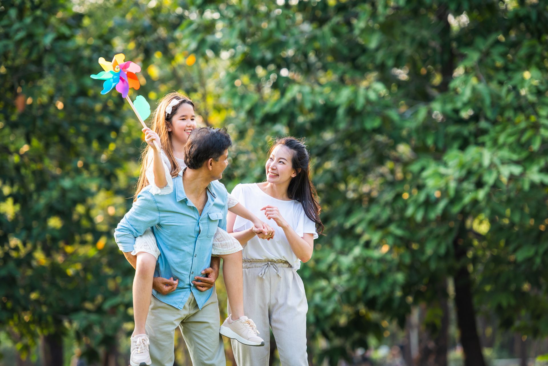 Three people walking outdoors in a green park, smiling and holding colorful pinwheels.