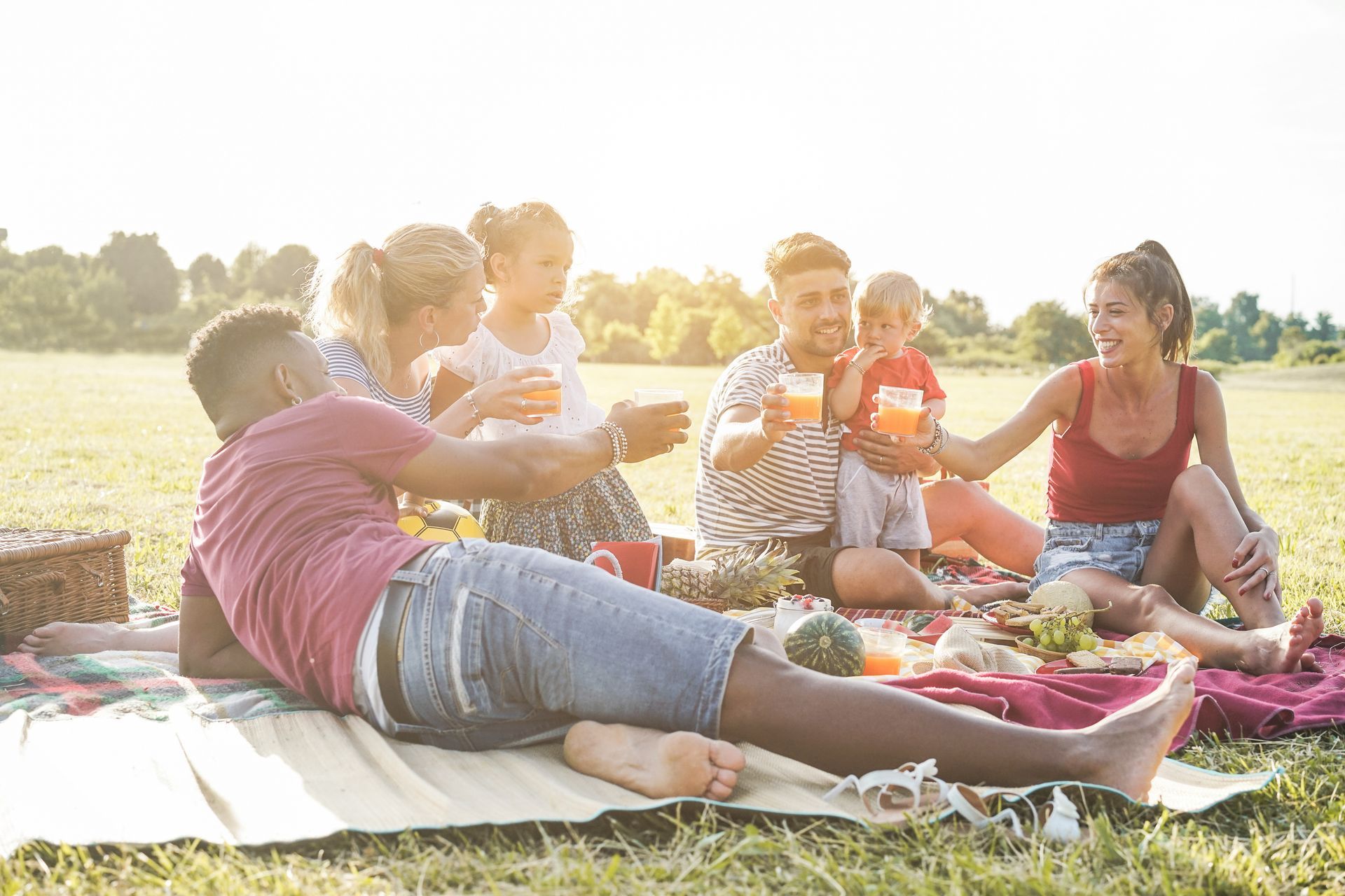 Friends picnicking on a blanket in a sunny park, sharing food and drinks