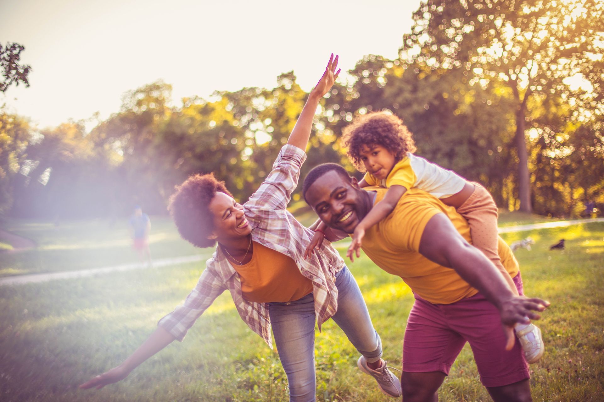 Friends playing in a sunlit park, laughing as one gives another a piggyback ride.