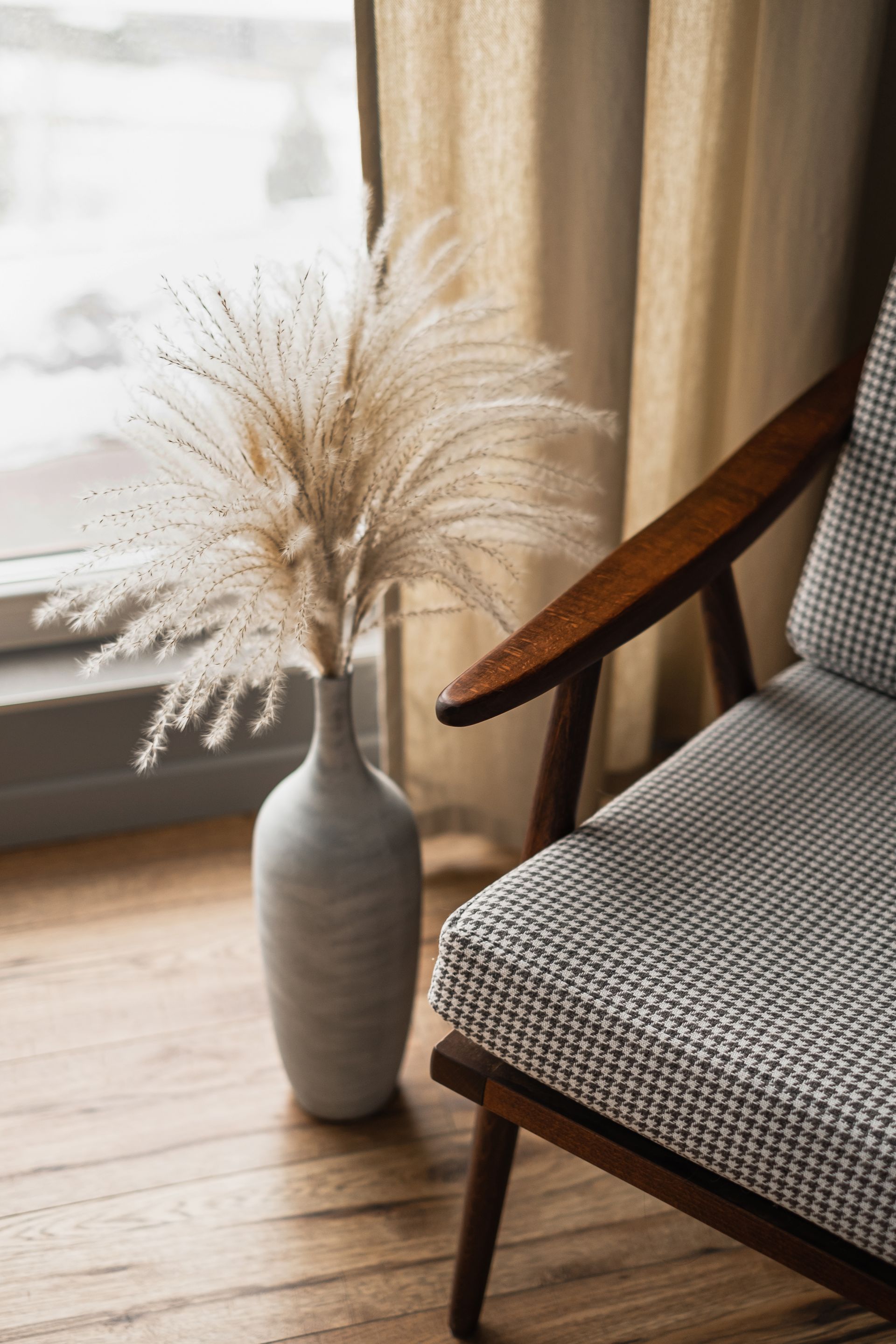 Vase with dried pampas grass beside a wooden chair in a sunlit room