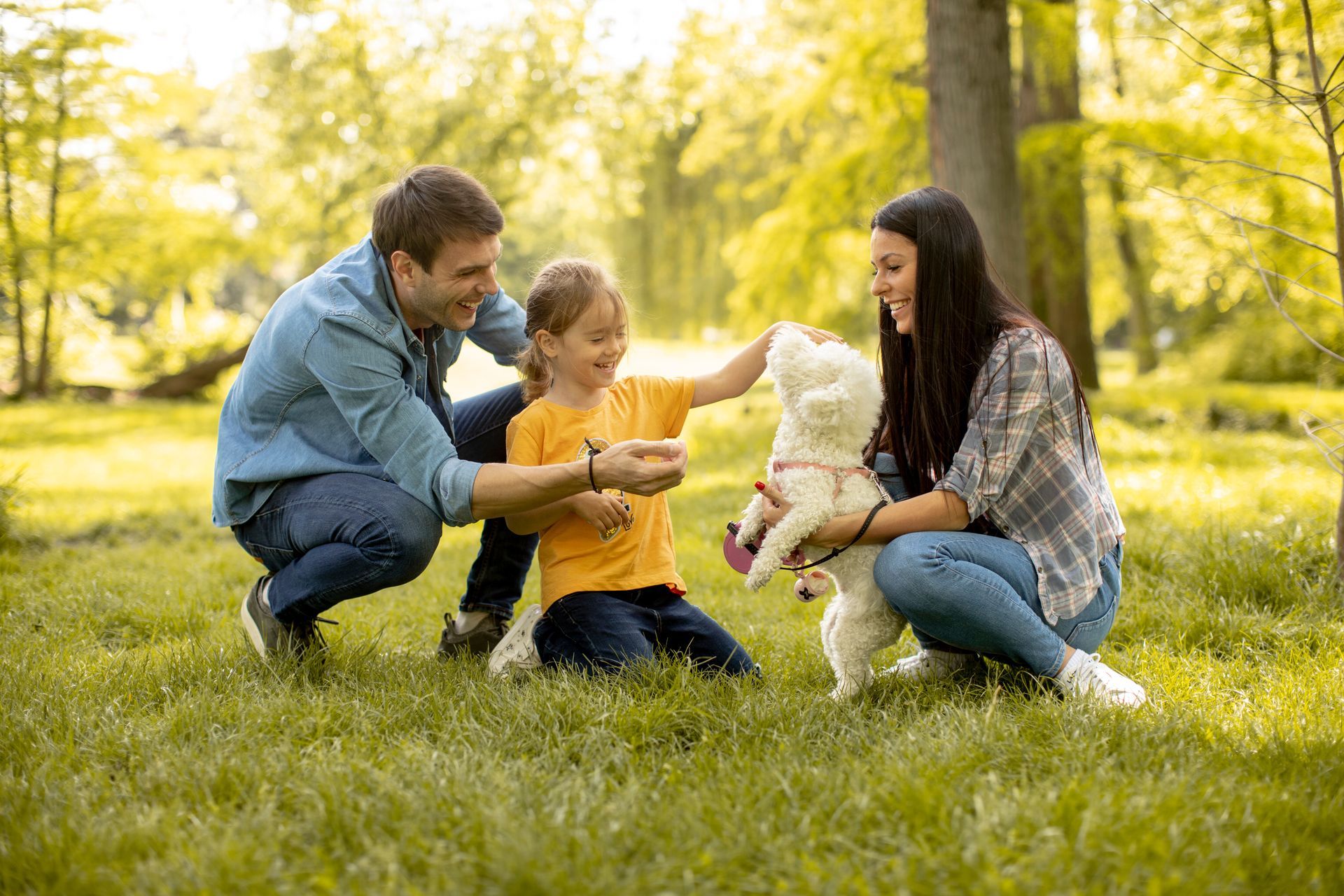 Family crouching on grass with a white dog in a sunny park