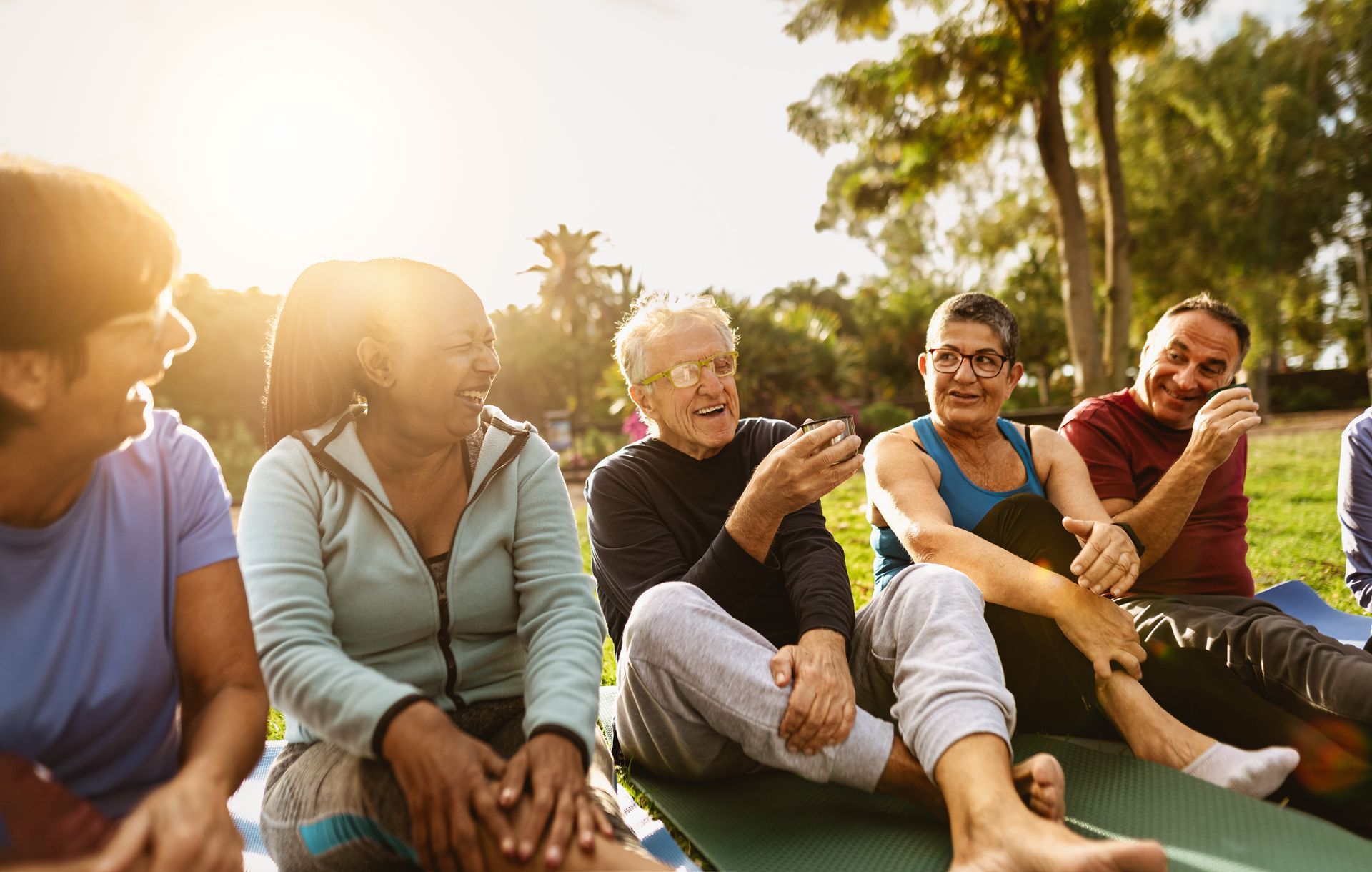 Friends sitting on blankets in a sunny park, chatting and smiling during a relaxed outdoor gathering.