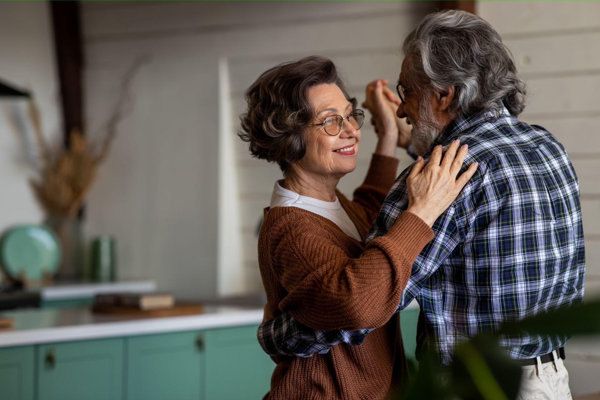 Two people carrying boxes and a potted plant through a hallway, smiling while moving in.