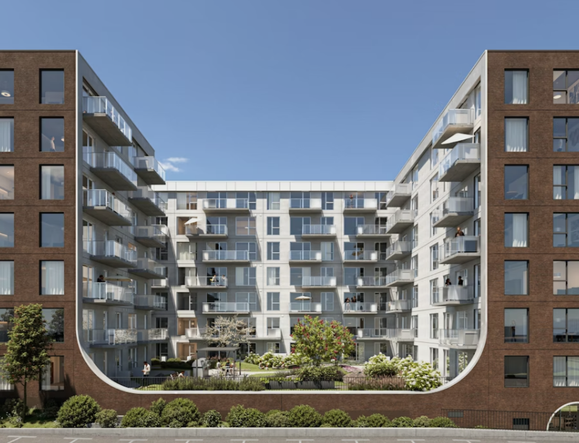 Immeuble d'appartements en forme de U, extérieur en briques, balcons et jardin intérieur sous un ciel bleu.