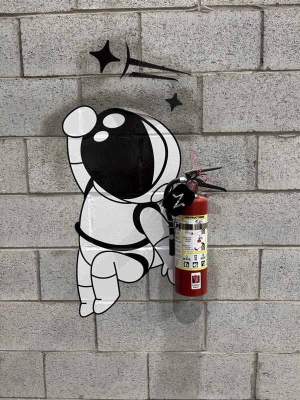 Cartoon astronaut graffiti on a gray brick wall beside a red fire extinguisher