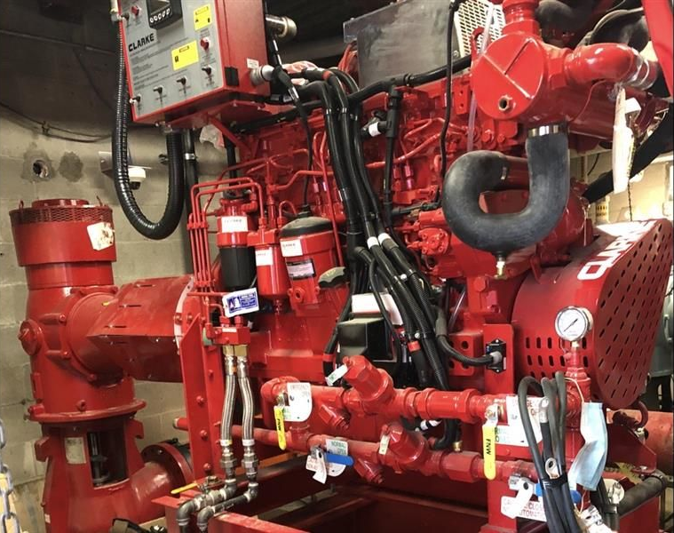 Red industrial engine with red pipes, valves, and black hoses in a mechanical room