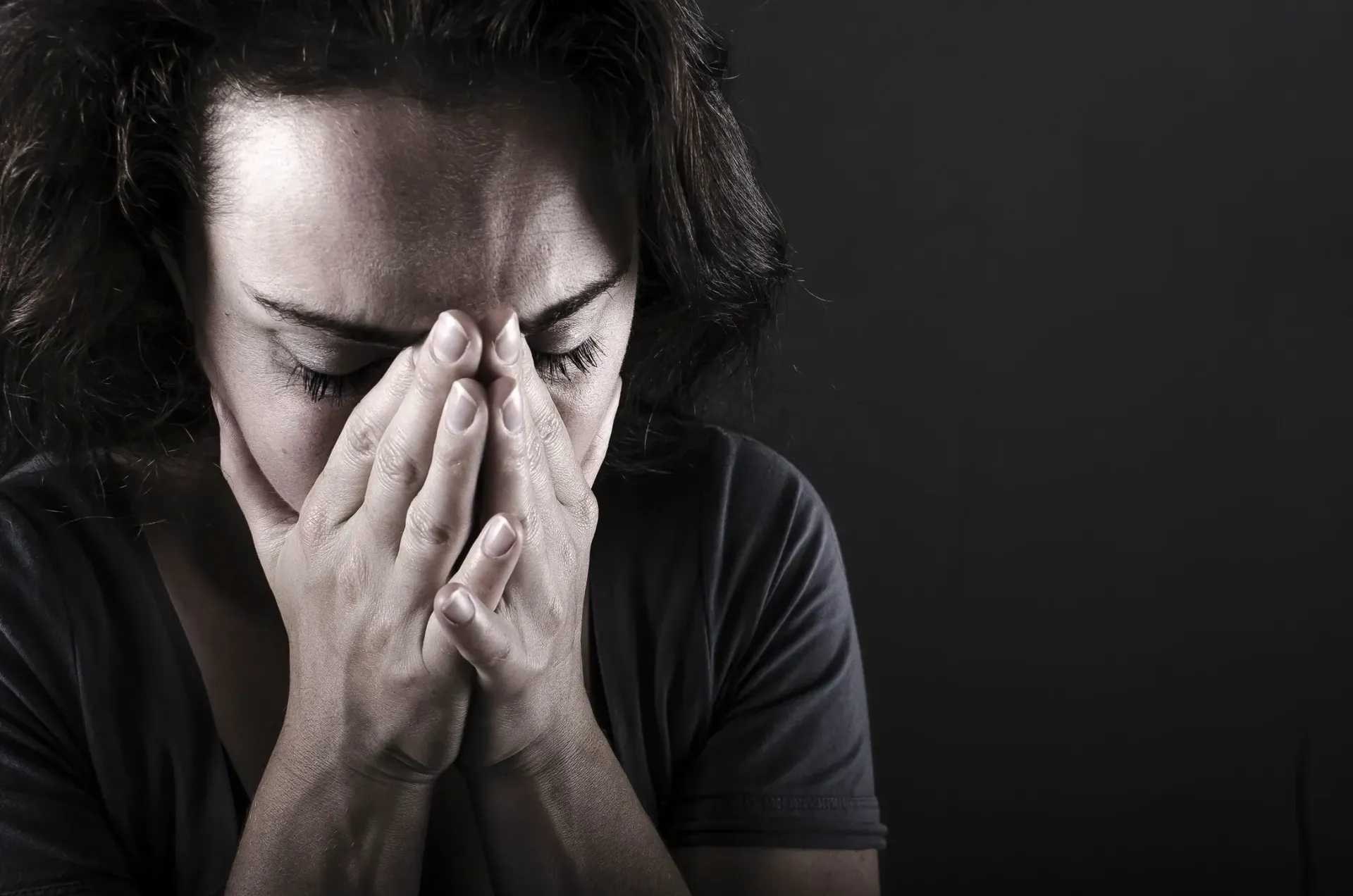 Person with hands over face in a dark setting, appearing distressed or overwhelmed