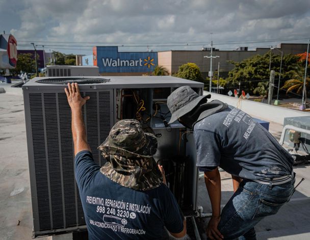 Two workers crouch beside a rooftop HVAC unit, with a Walmart store sign in the background.