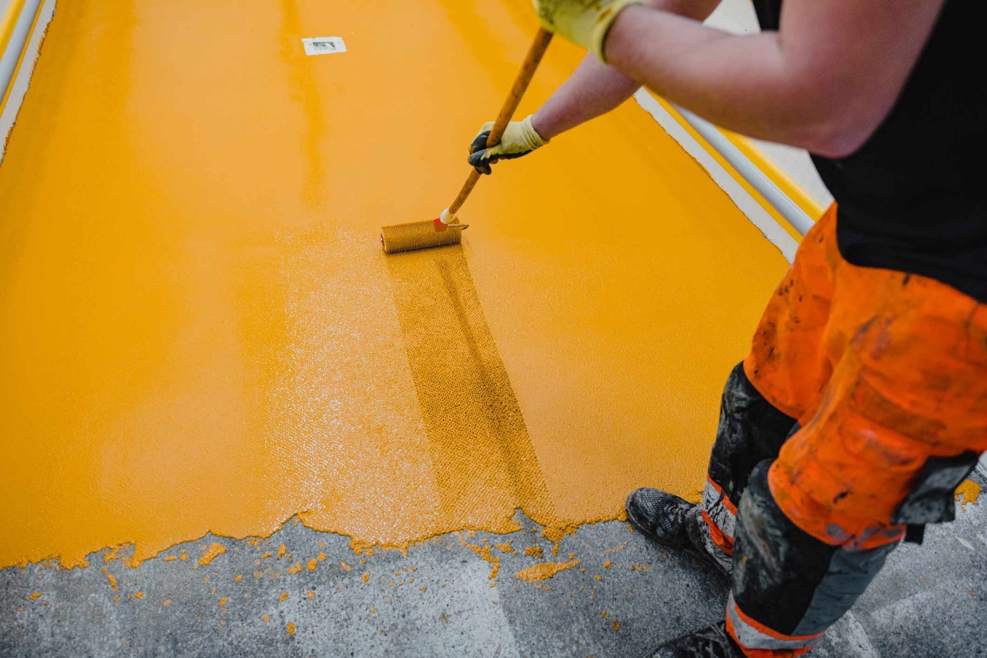 A man is painting a yellow floor with a roller.