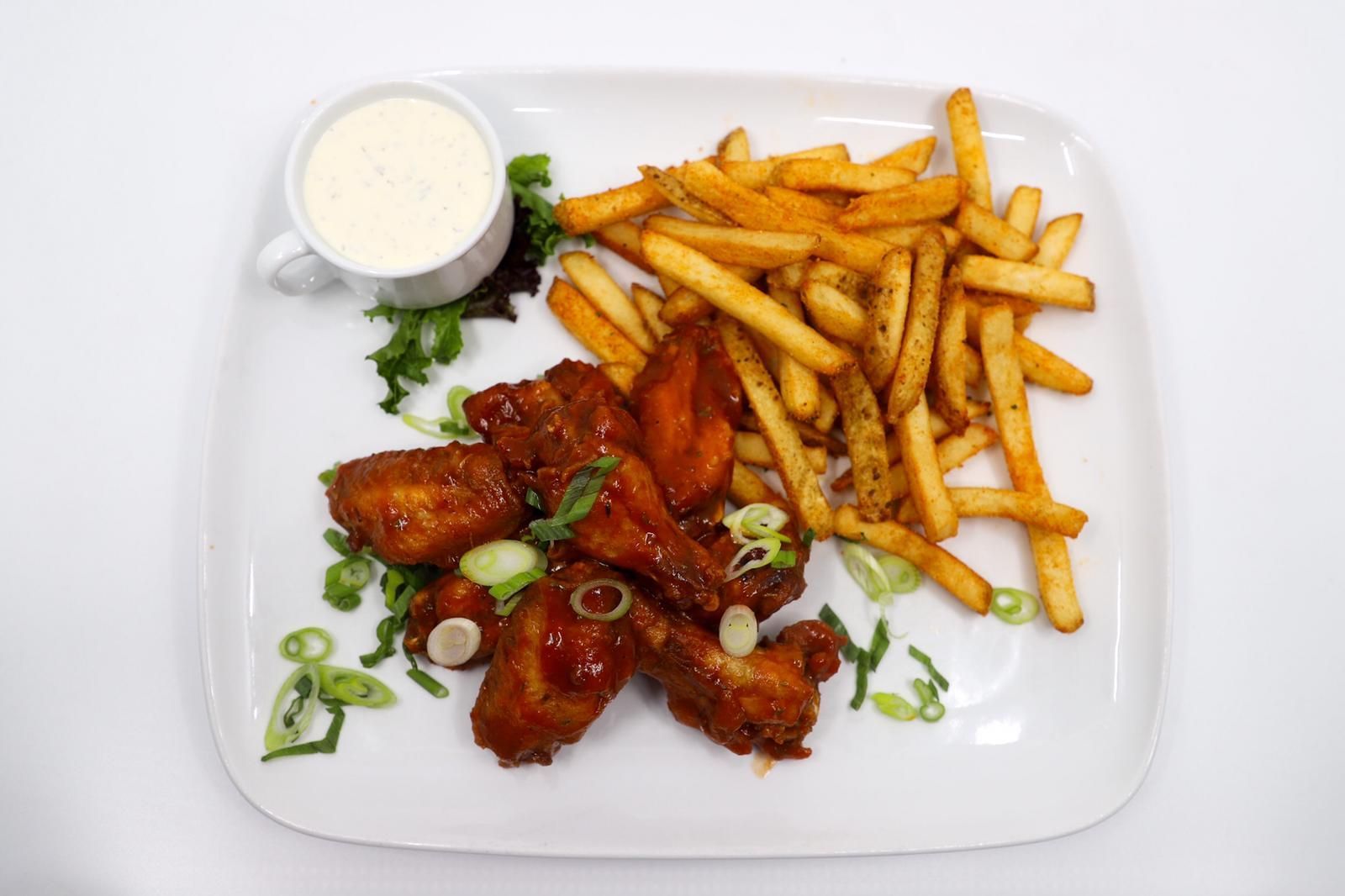 A white plate topped with chicken wings and french fries.