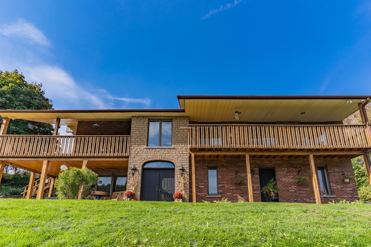 A large brick house with a large porch is sitting on top of a lush green hill.