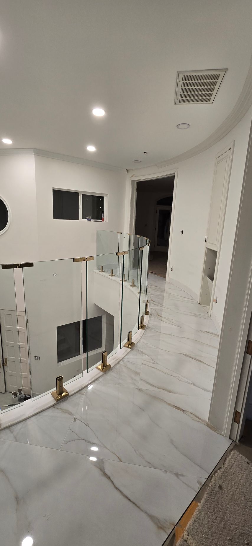 Interior view of a modern hallway with glass railings, white walls, and marble flooring.