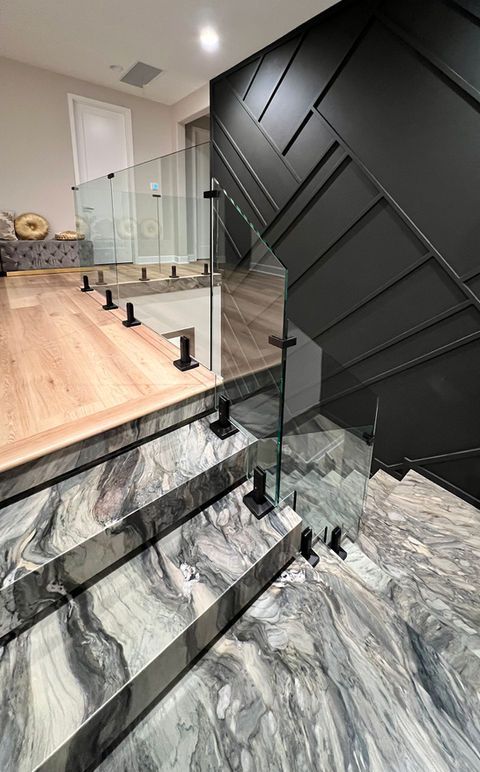 Staircase with marble steps, glass railing, and black panel wall. Wooden flooring on the landing.