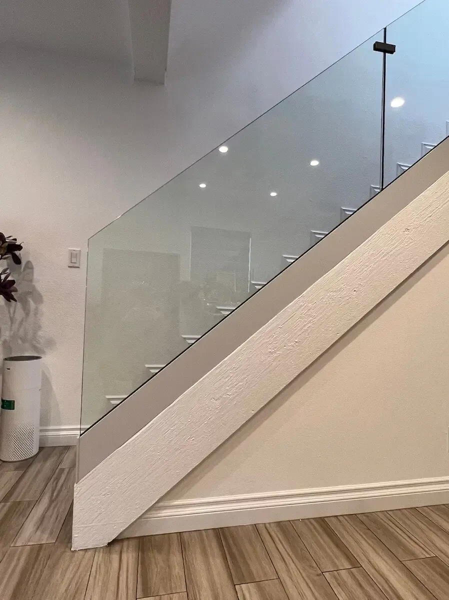 Staircase with glass railing, white walls, and light wooden floor.