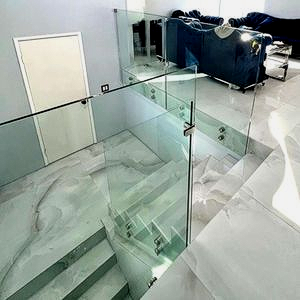Modern interior with glass railing, marble-look flooring, and a staircase leading to a living area with blue sofas.