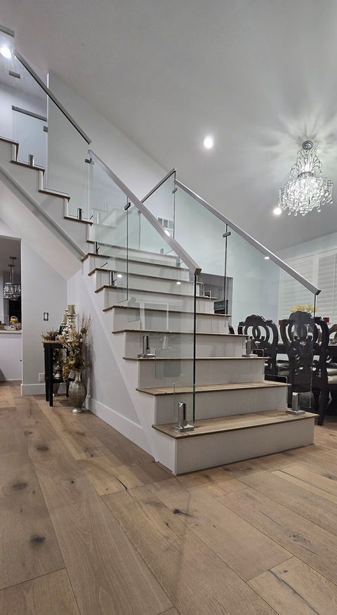 Modern staircase with glass railing and light wood flooring.