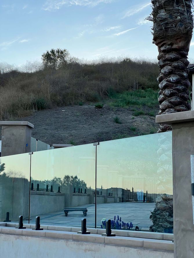 Glass fence in front of a concrete structure, with a hillside and palm tree in the background.