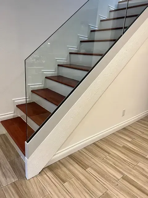 Staircase with wooden steps and glass railing, white risers, and wood-look flooring.