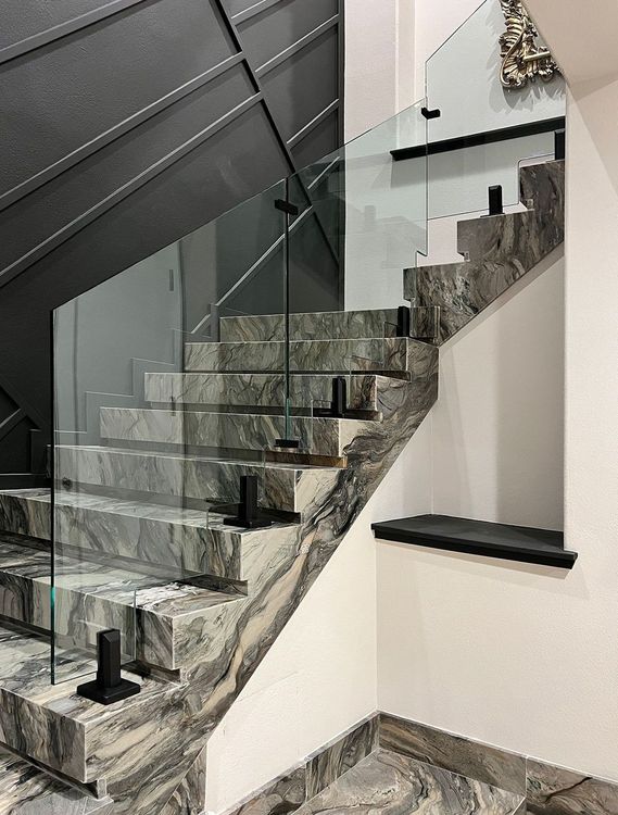 Staircase with marble steps, glass railing, and black supports.
