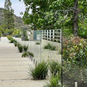 A modern outdoor walkway with glass barriers and greenery against a natural backdrop.