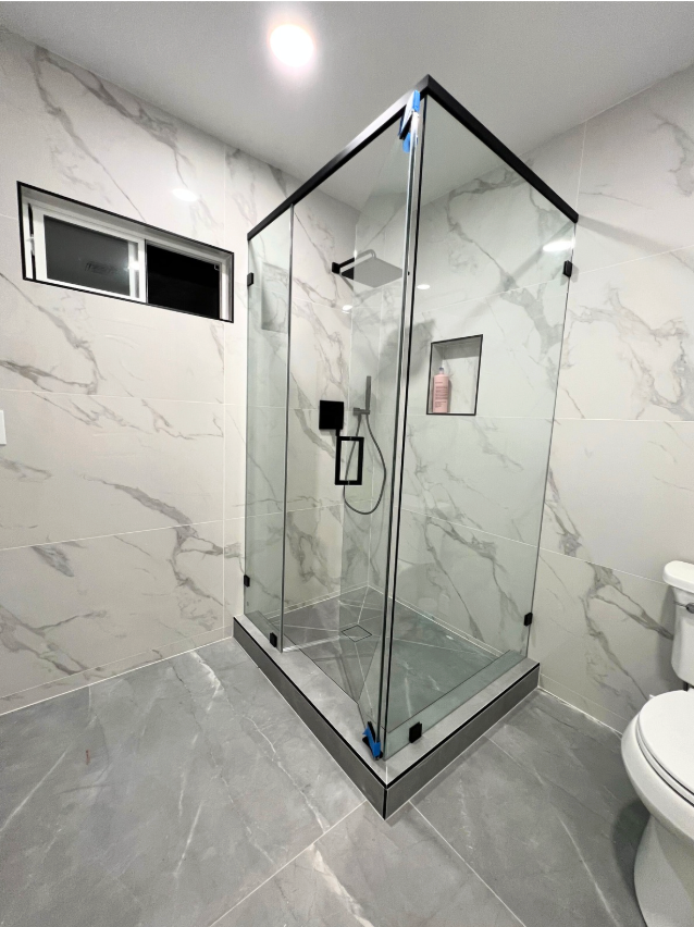 Modern bathroom with glass shower enclosure, marble-look tiled walls, and gray floor.