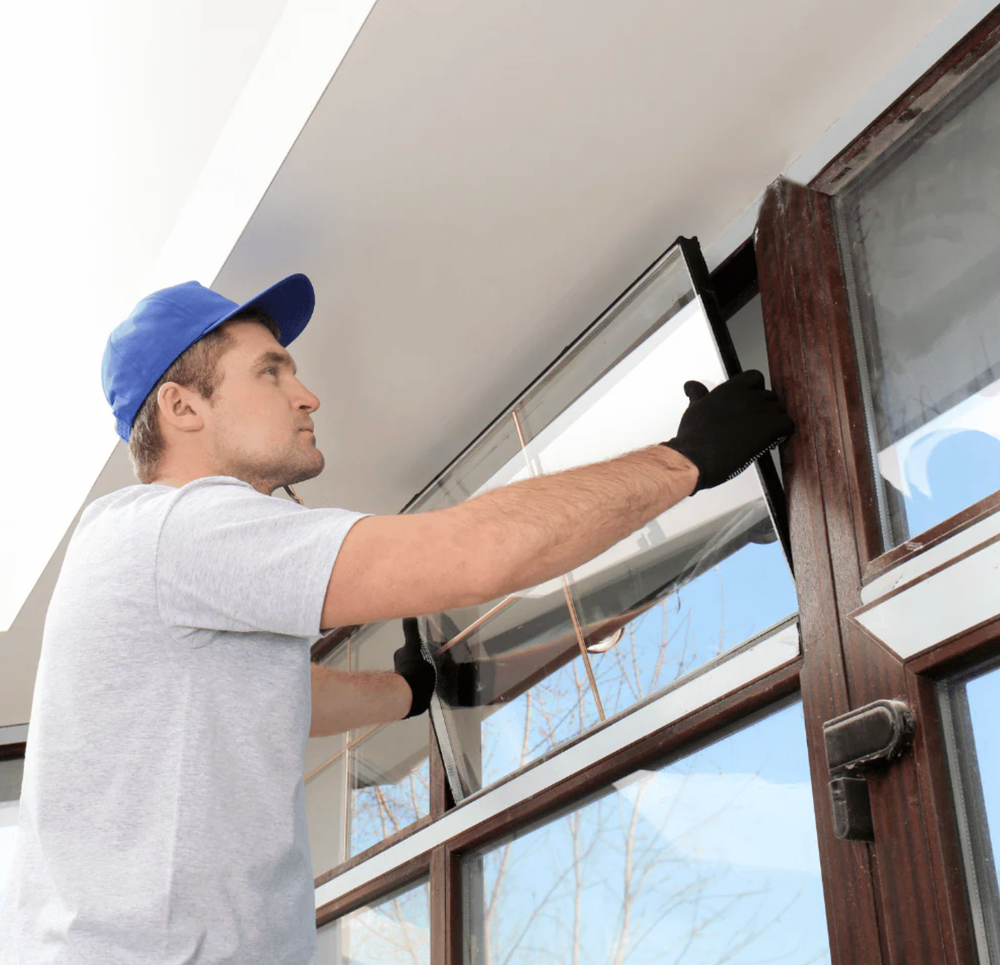 Man in blue cap and black gloves installing a window screen.