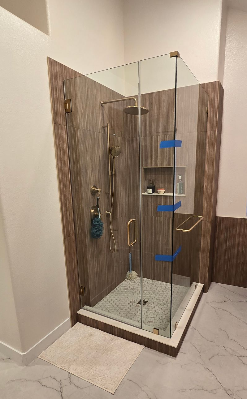 Bathroom with a clear glass shower, white walls, and wooden accents.
