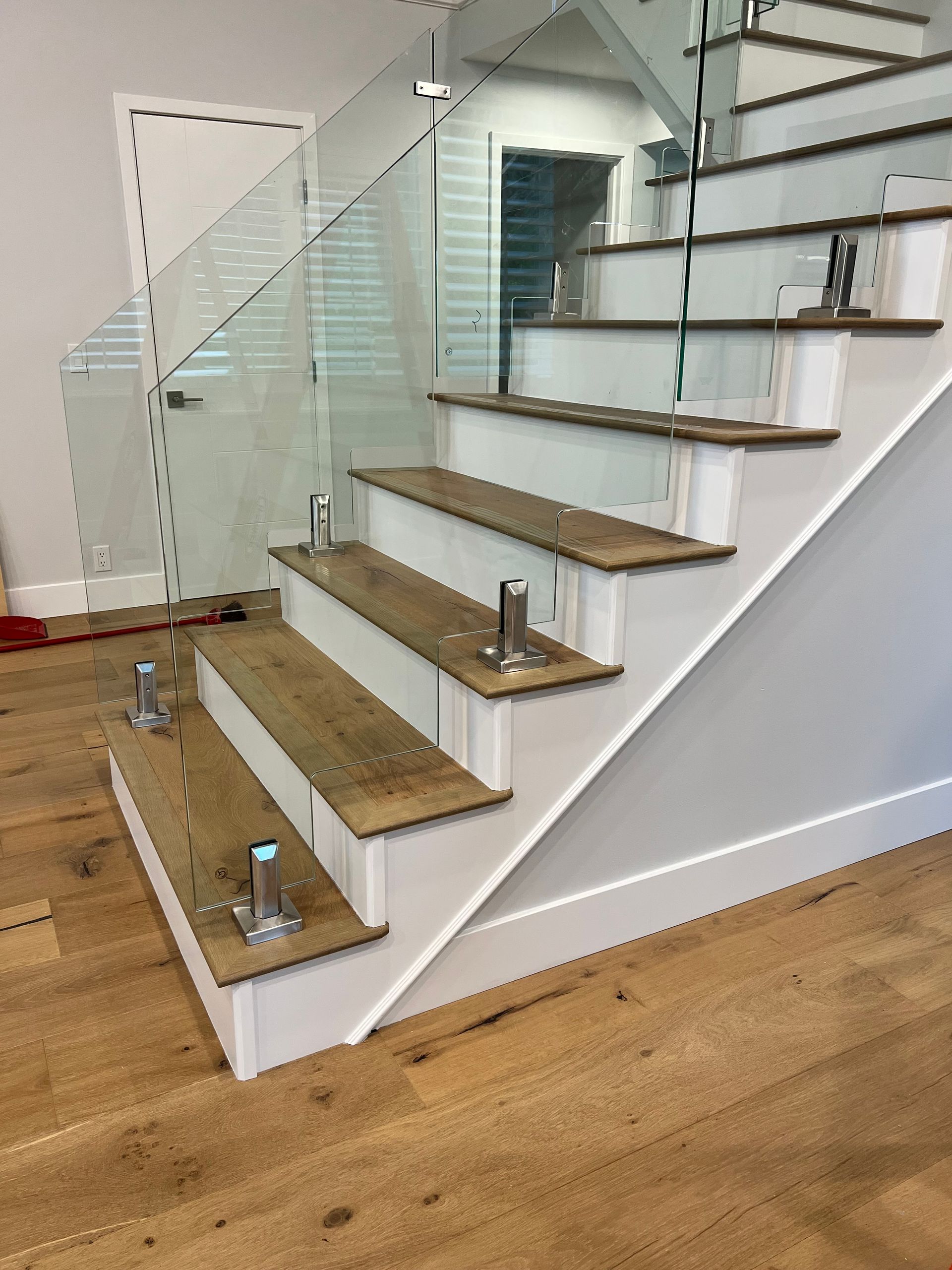 Staircase with wooden steps and glass railing, stainless steel posts. White risers and trim.