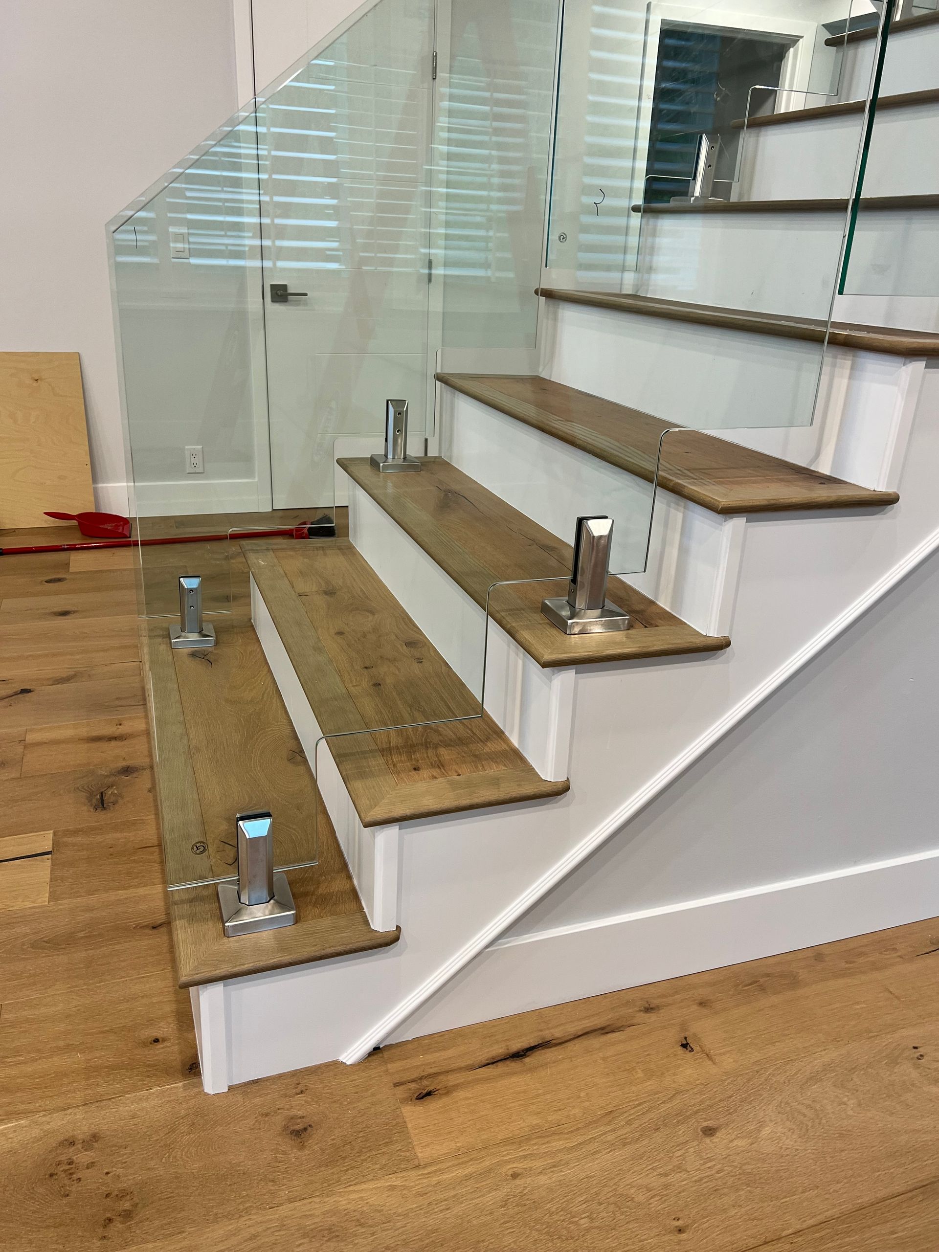 Staircase with wood steps and glass railing, stainless steel supports, white trim.
