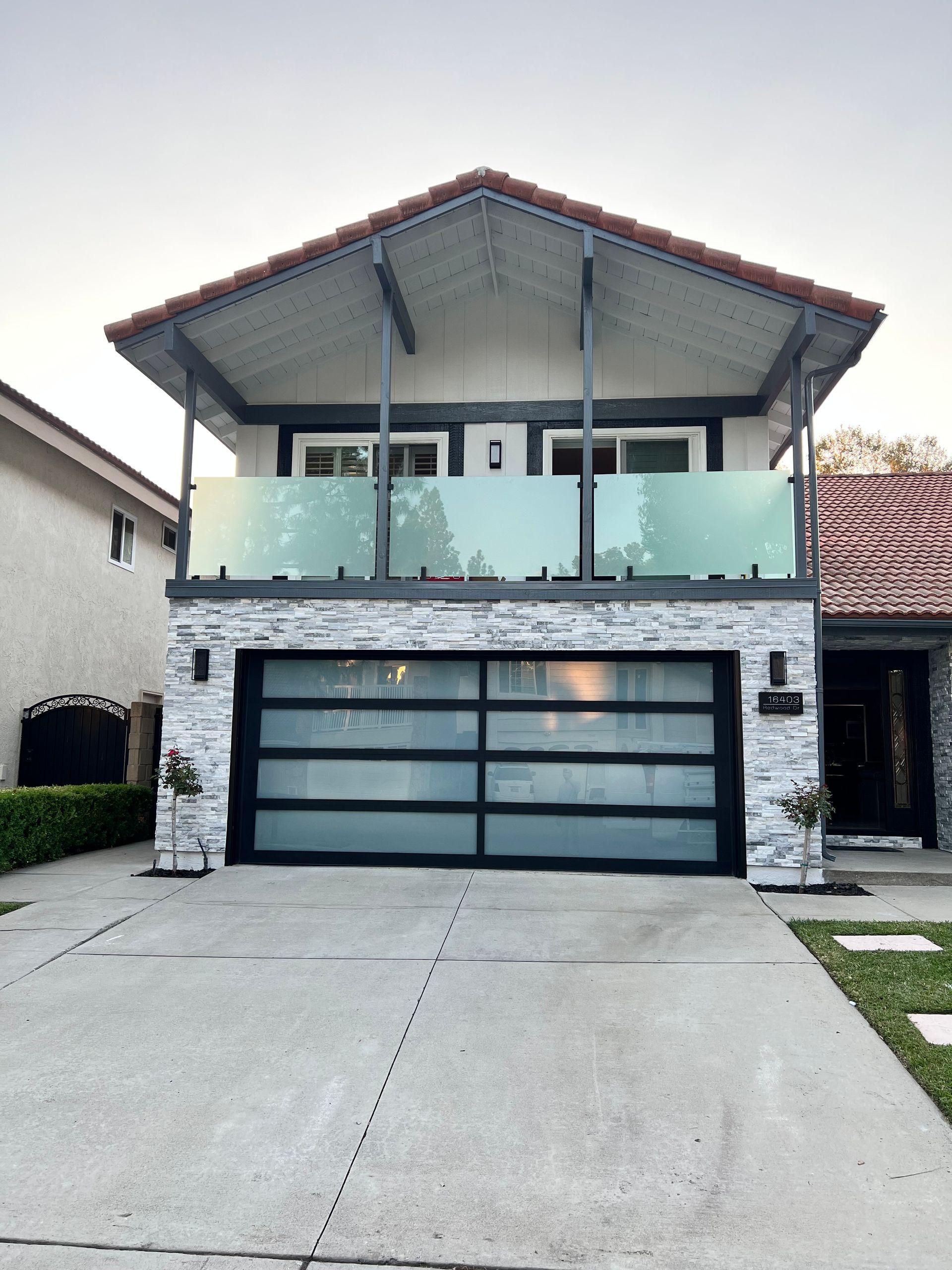 Two-story house with frosted glass garage door and balcony with glass panels. White and grey exterior.