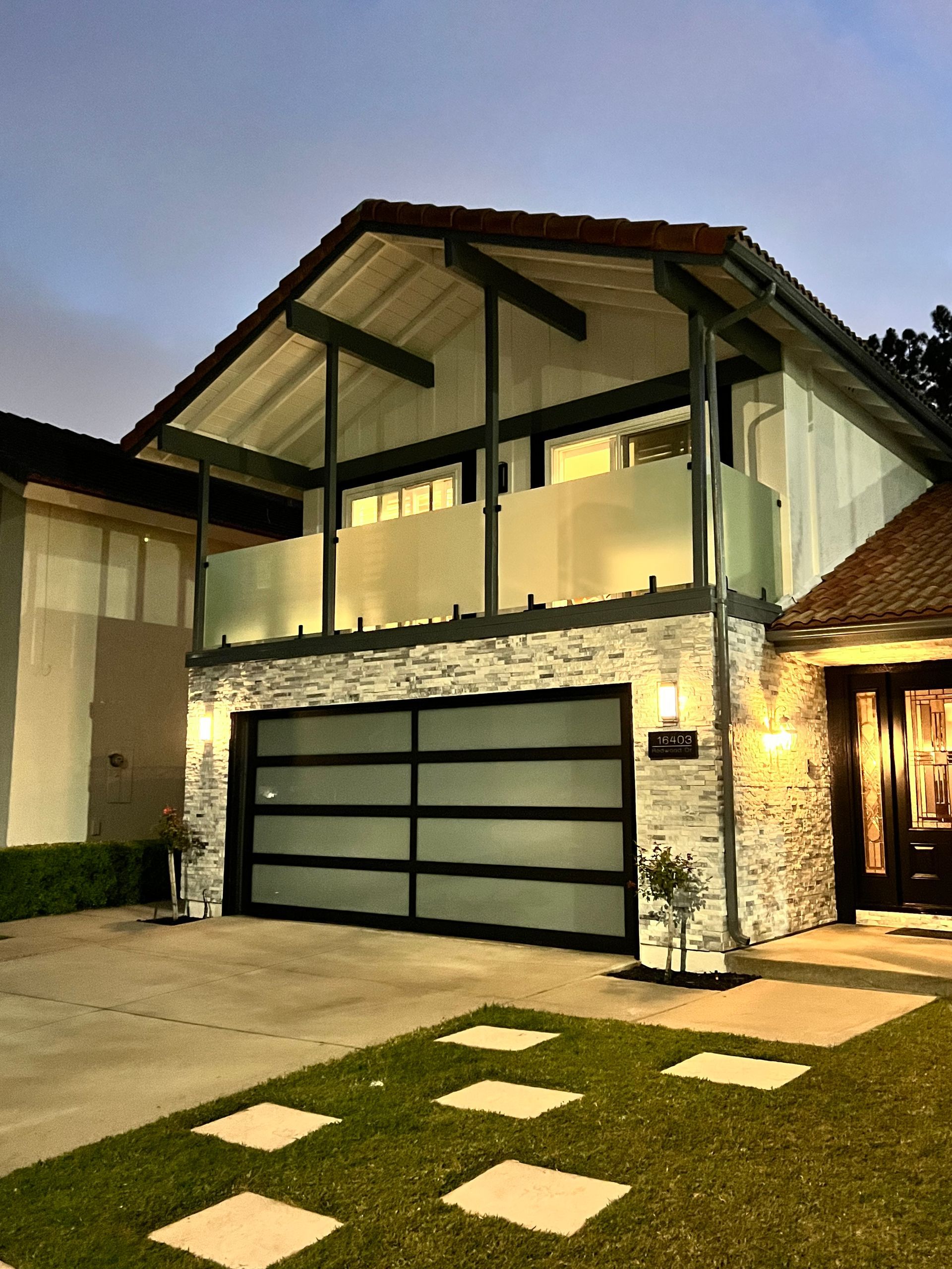 House exterior with stone facade, glass garage door, and balcony.