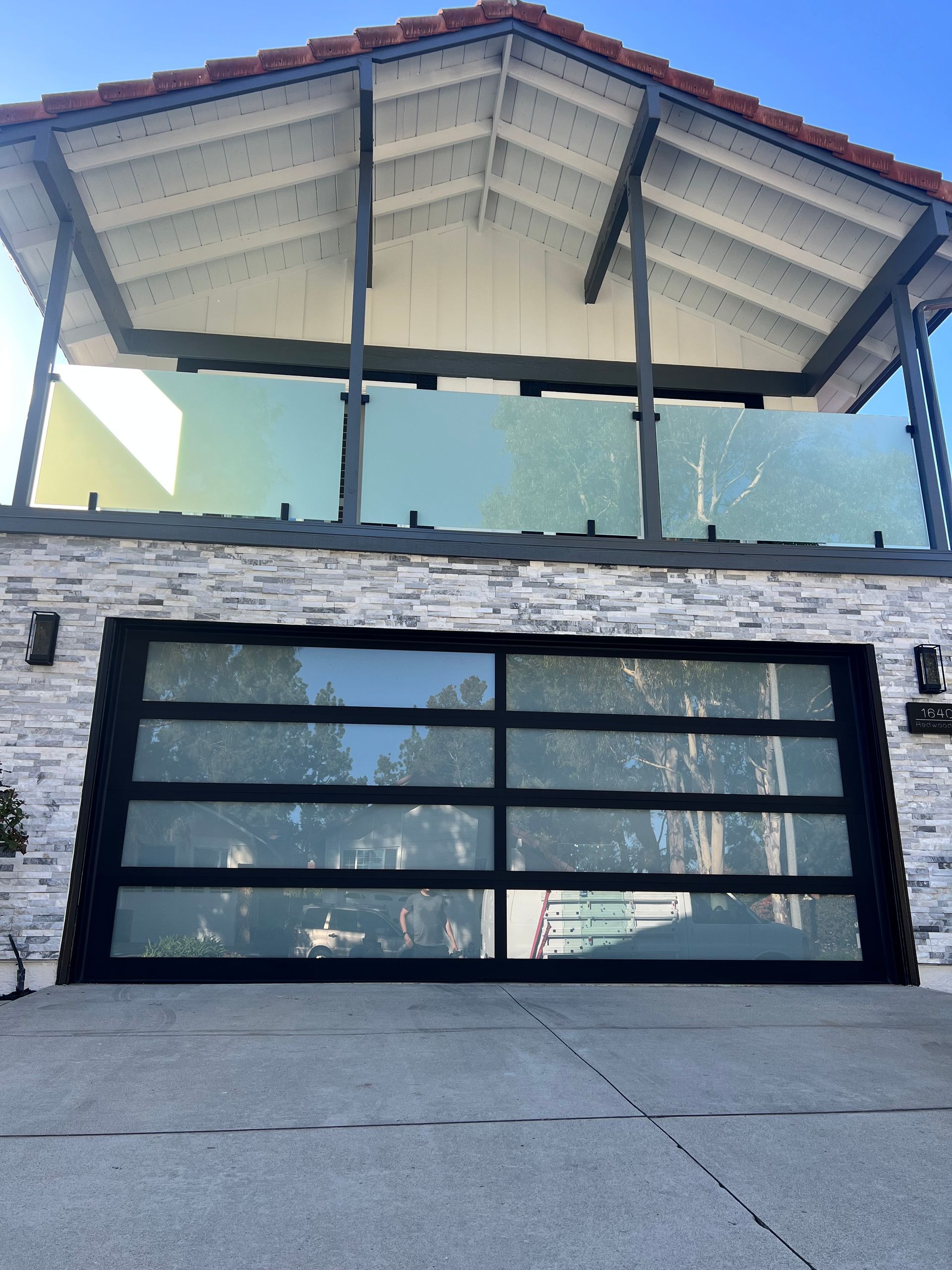 Modern home exterior with glass garage door and balcony with glass railing.