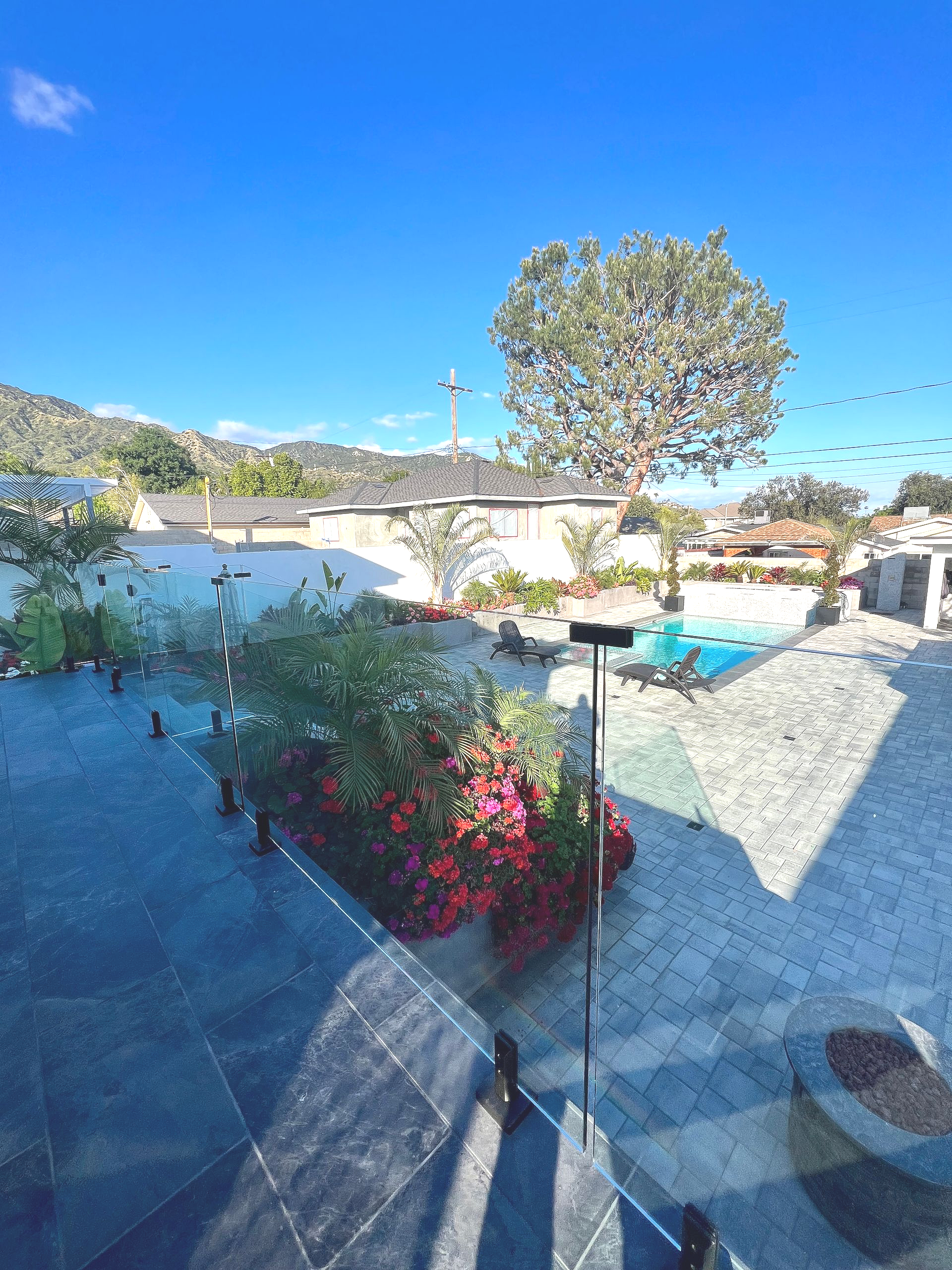A sunny outdoor scene with a garden, buildings, and a large tree under a bright blue sky.